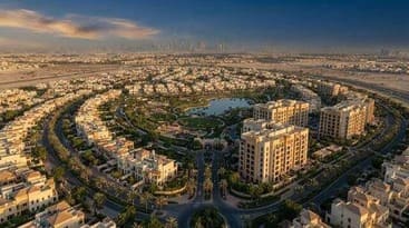 Aerial view of a landscaped residential neighborhood with a central pond and distant skyscraper skyline.